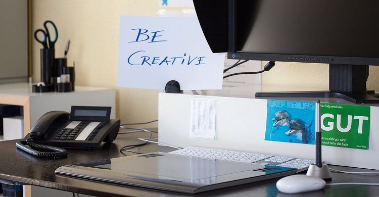 /pt/images/image-of-a-desk-with-a-monitor-laptop-mouse-and-phone-on-it-and-a-sign-that-says-be-creative-on-the-wall.jpg