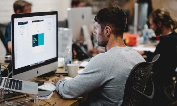/pt/images/man-in-sweatshirt-sitting-at-desk-working-on-computer.jpg