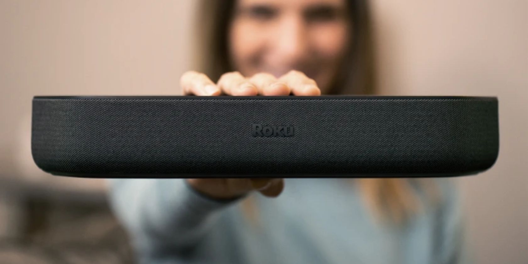 /sv/images/woman-standing-out-of-focus-holding-up-roku-streambar.jpg